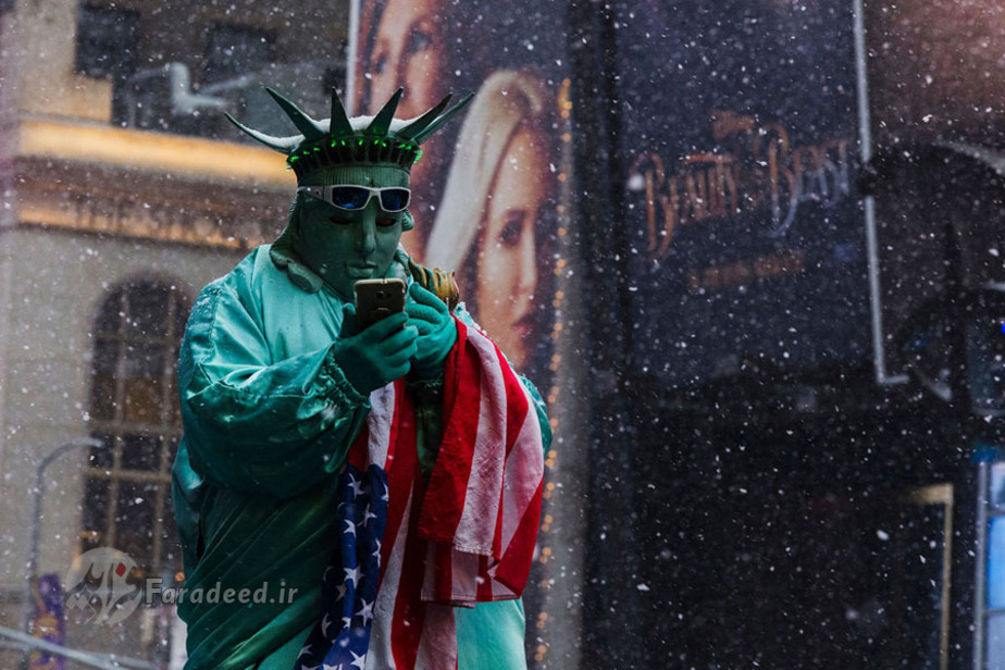 مردی با لباسی شبیه به مجسمه آزادی منتظر توریست‌ها است که زیر بارش برف در میدان تایمز با او عکس بگیرند